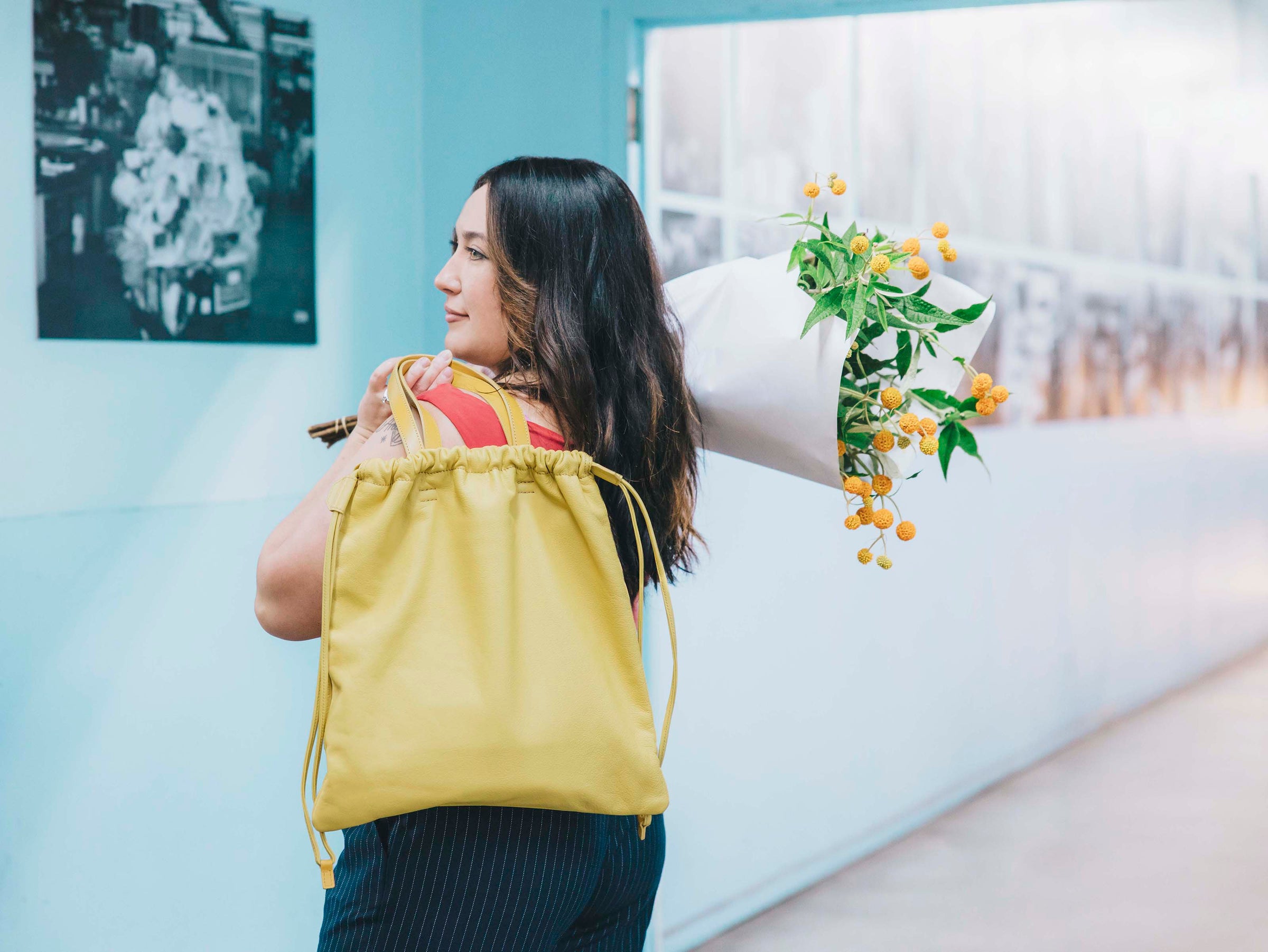 Tsuchiya Kaban’s ambassador Ren MacDonald carrying a bouquet of yellow flowers over her shoulder and wearing a Tsuchiya Kaban’s Ruffle Drawstring Tote in Yellow on her back.