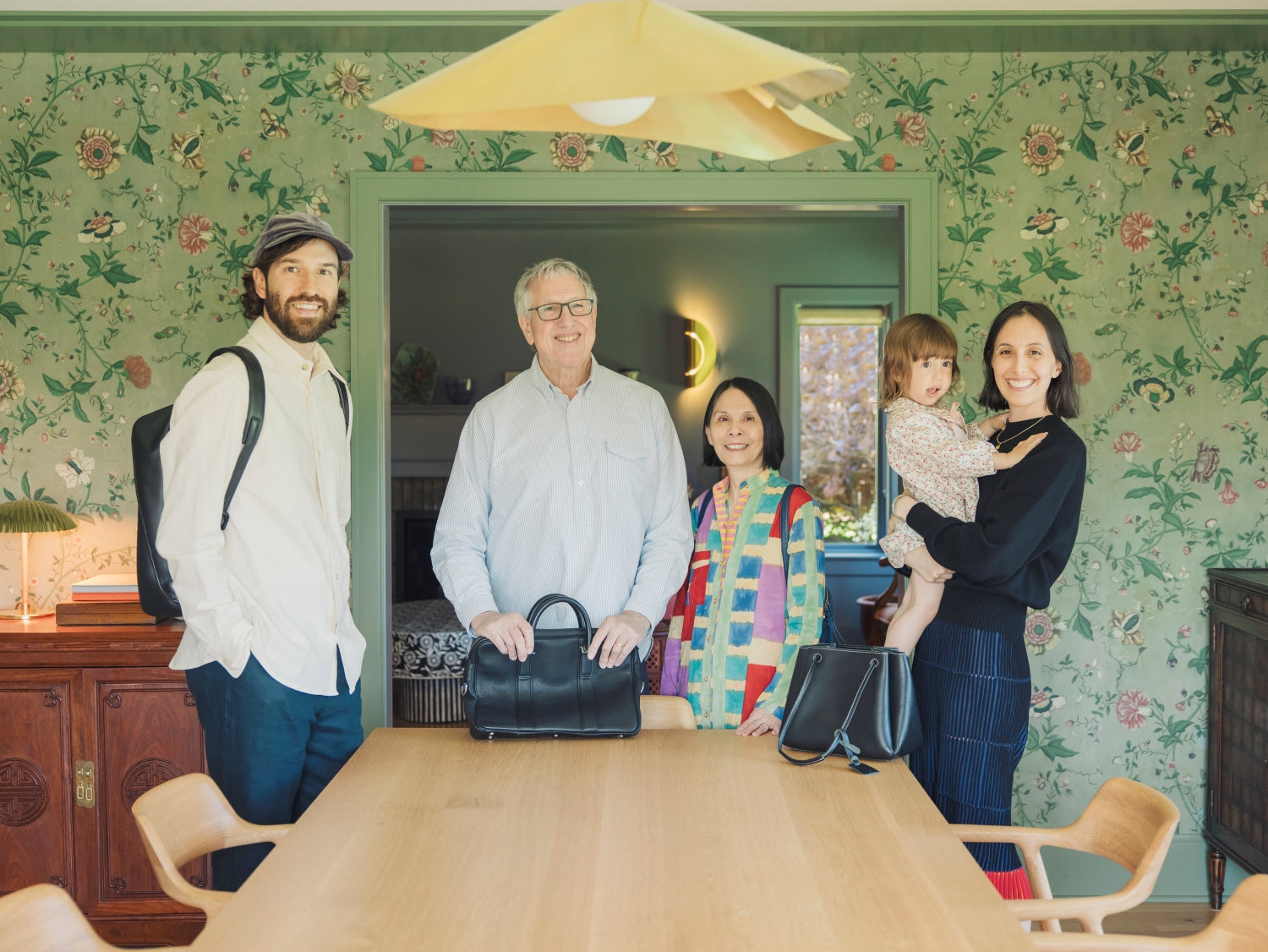 Three-generation family smiling at the camera, each carrying a Tsuchiya Kaban leather bag.