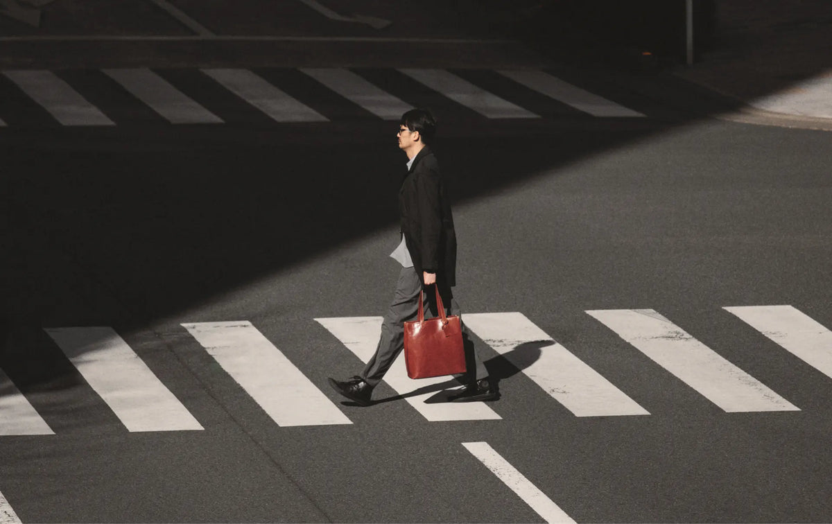 a man crossing the road carrying his Tsuchiya Kaban Leather Bag Diario Tall Tote in Brown