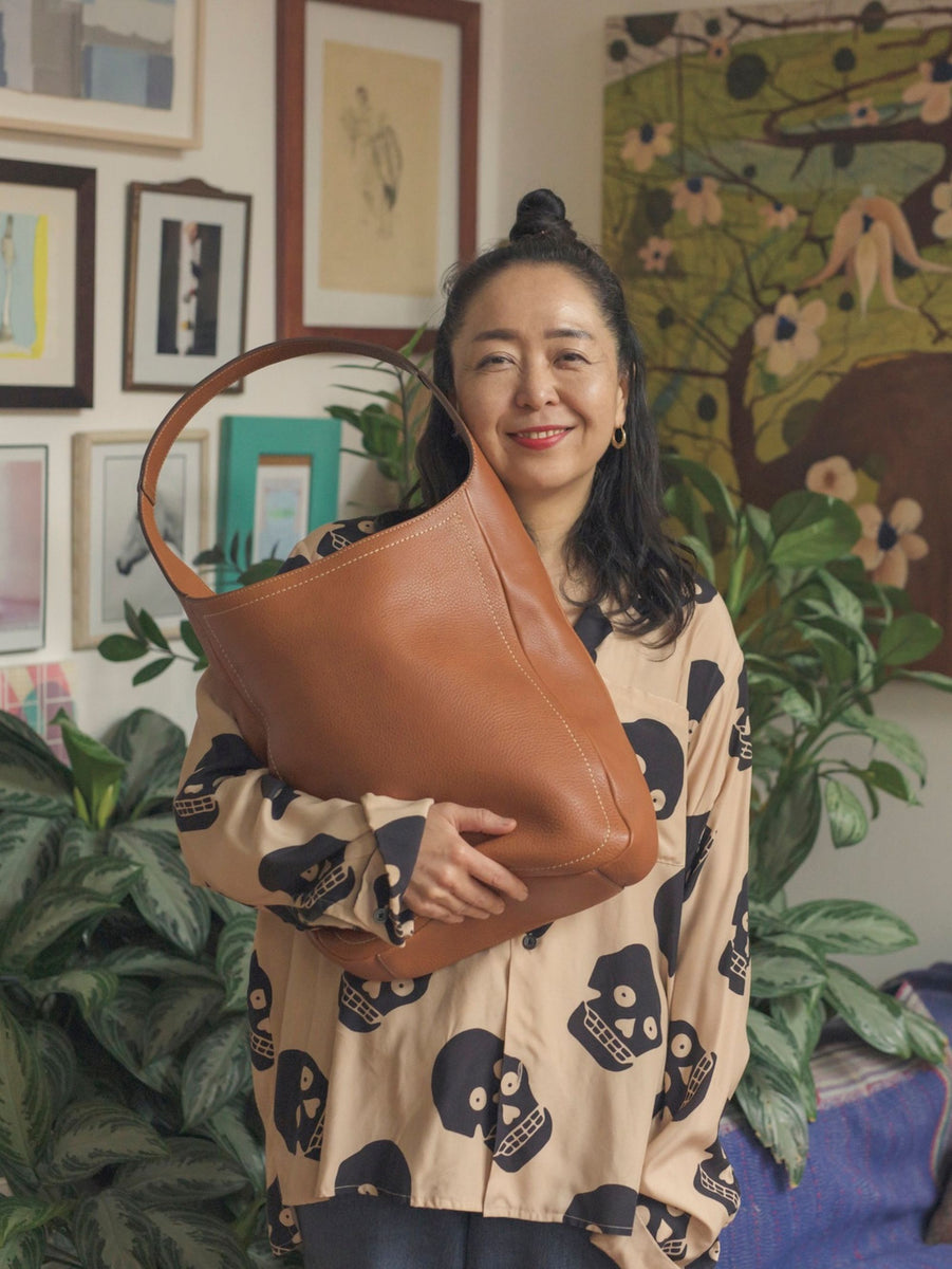 Ceramicist Shino Takeda smiling while holding her favorite Tone Nume One Shoulder Tote in Brown in her room.