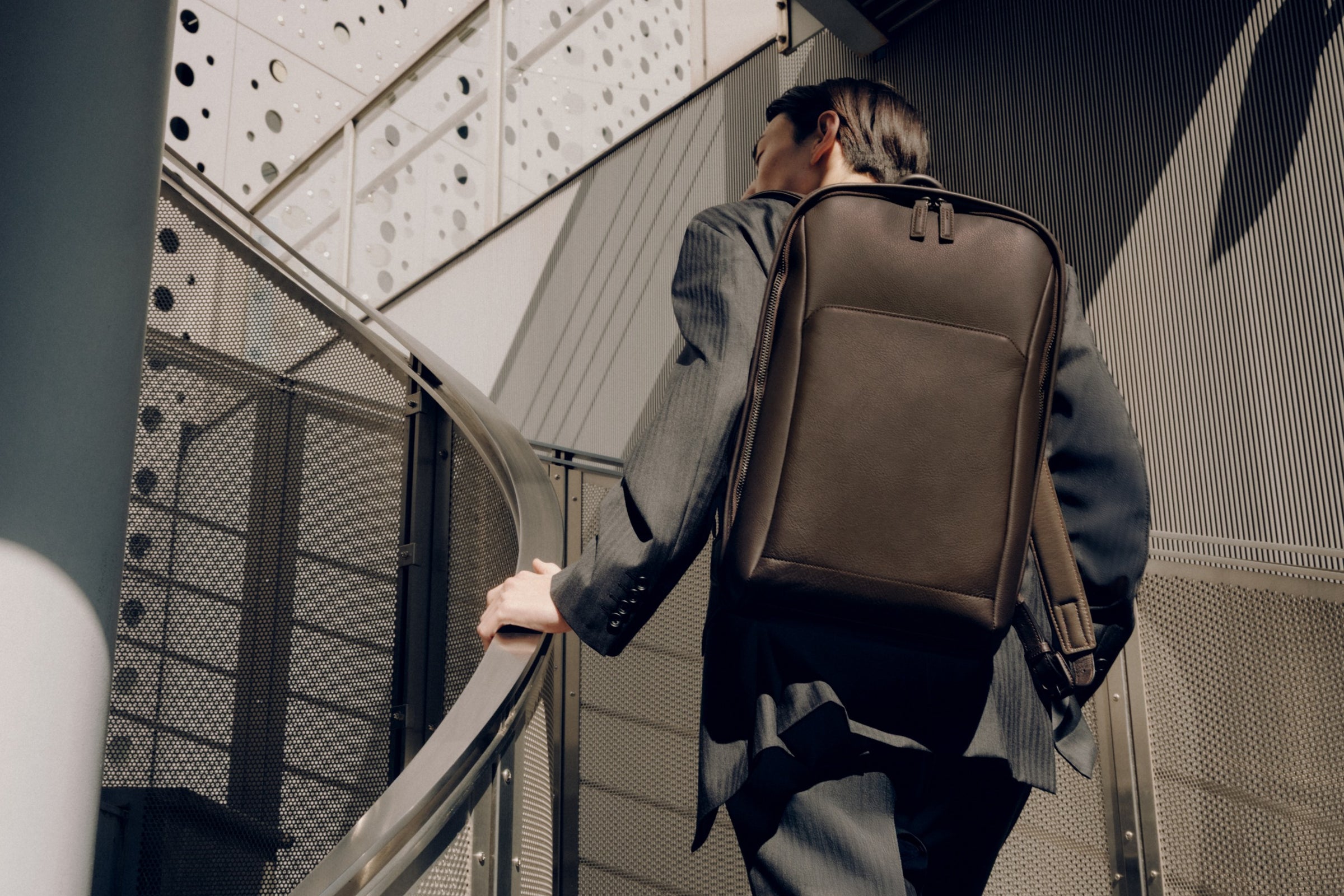 Man with a brown Vainno waterproof backpack walking up a staircase in an urban setting