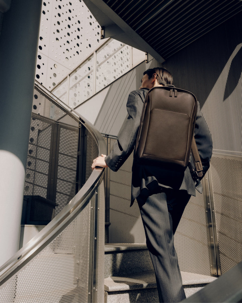 Man with a brown Vainno waterproof backpack walking up a staircase in an urban setting