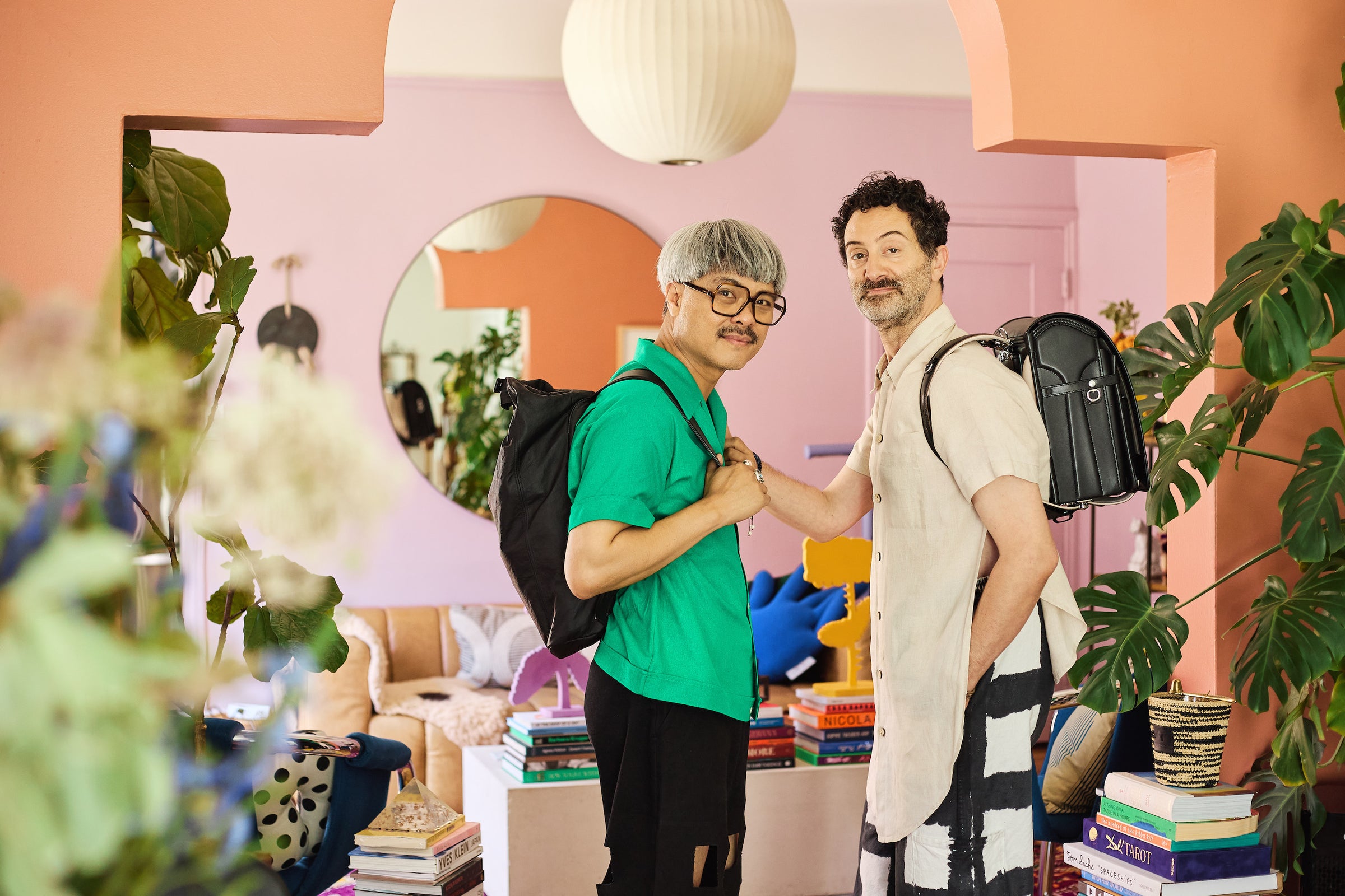 Tsuchiya Kaban’s ambassador Chelito Villaflor and Chris Albanese Owner of Eskina pose together in a colorful, stylish room, each wearing a Tsuchiya Kaban’s backpack. The space is filled with plants, books, and modern decor.