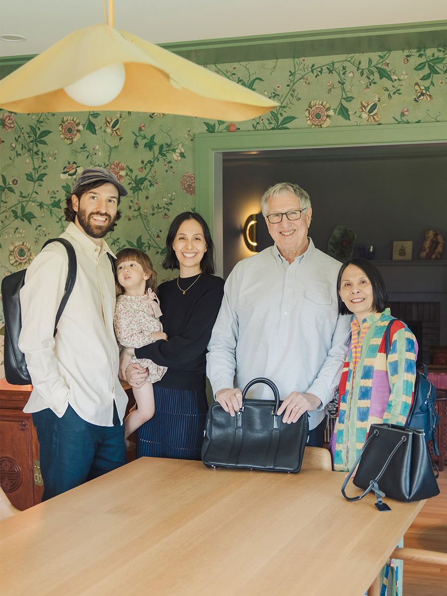 Three-generation family smiling at the camera, each carrying a Tsuchiya Kaban leather bag.